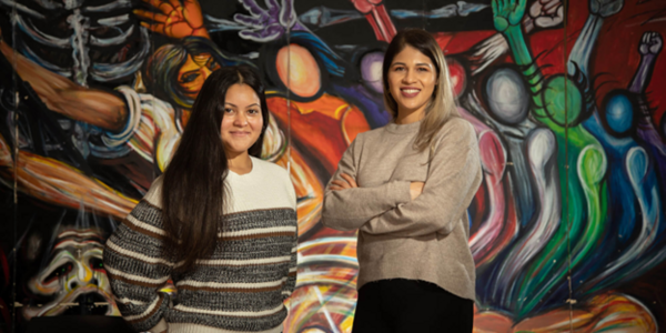 Two people standing in front of colorful wall.